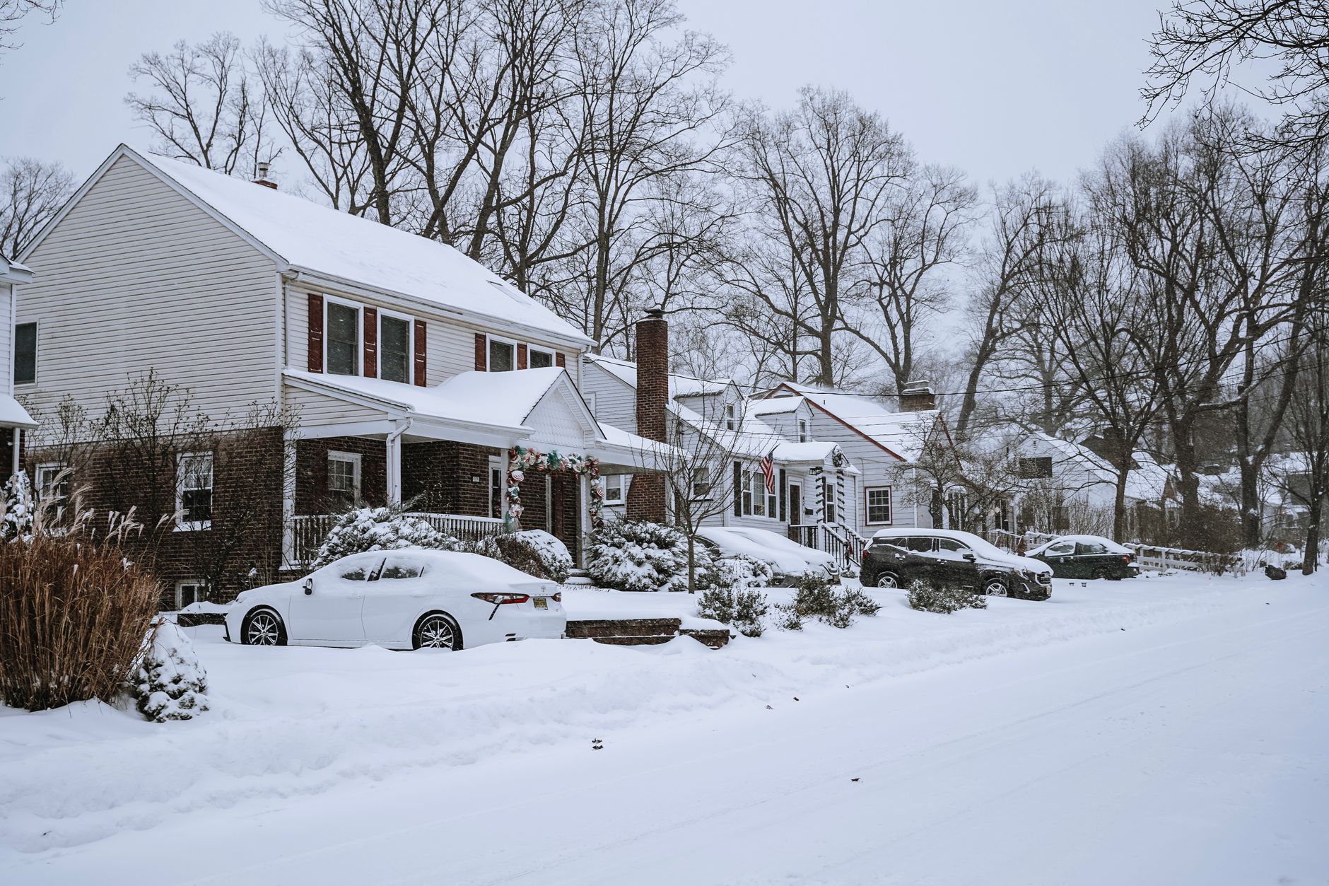 Snow-covered residential street with parked cars and bare trees