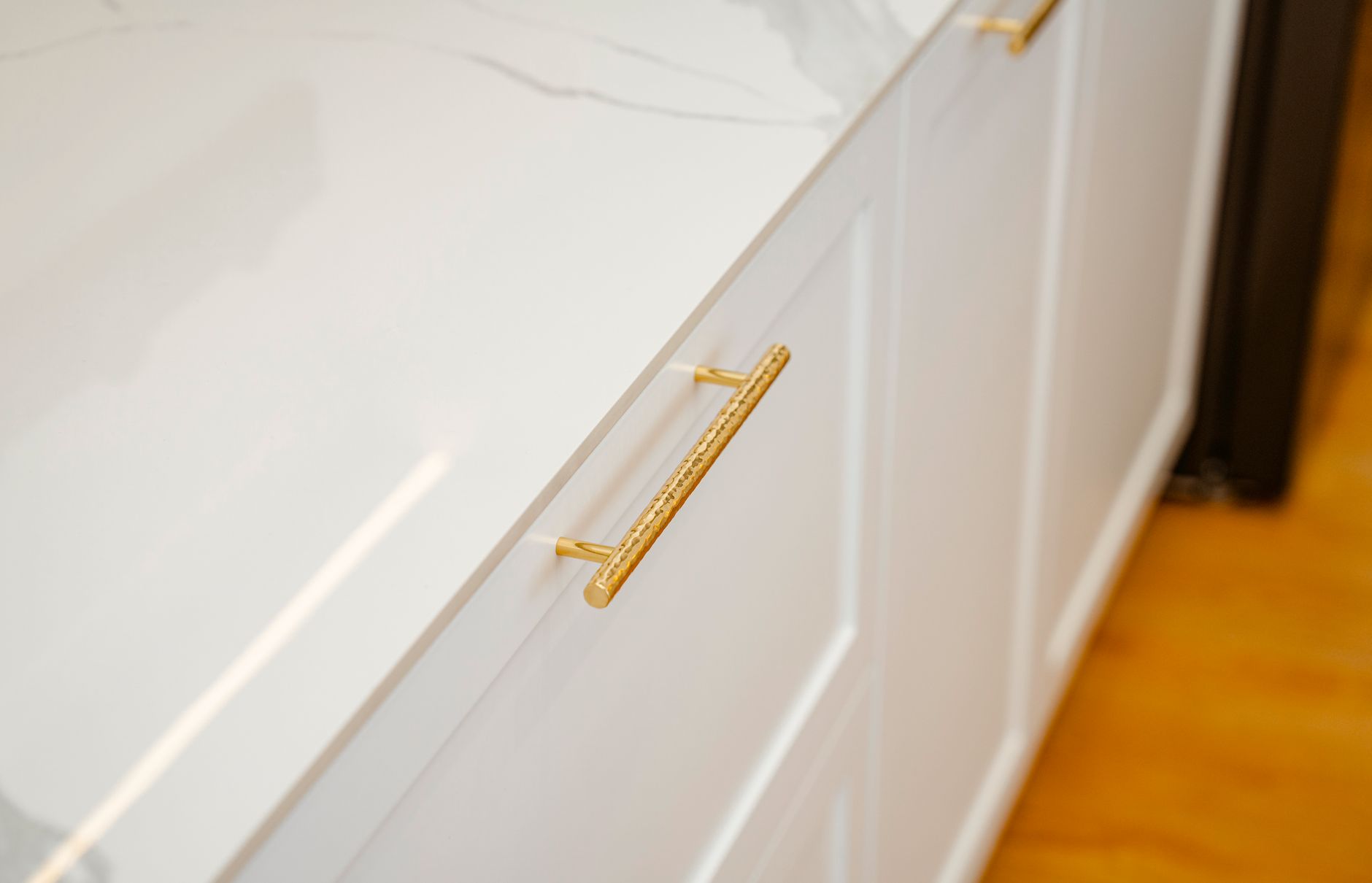 Close architectural detail of cabinetry, stone and warm metal hardware