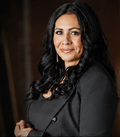Gina Sanchez in a dark blazer against a warm studio backdrop