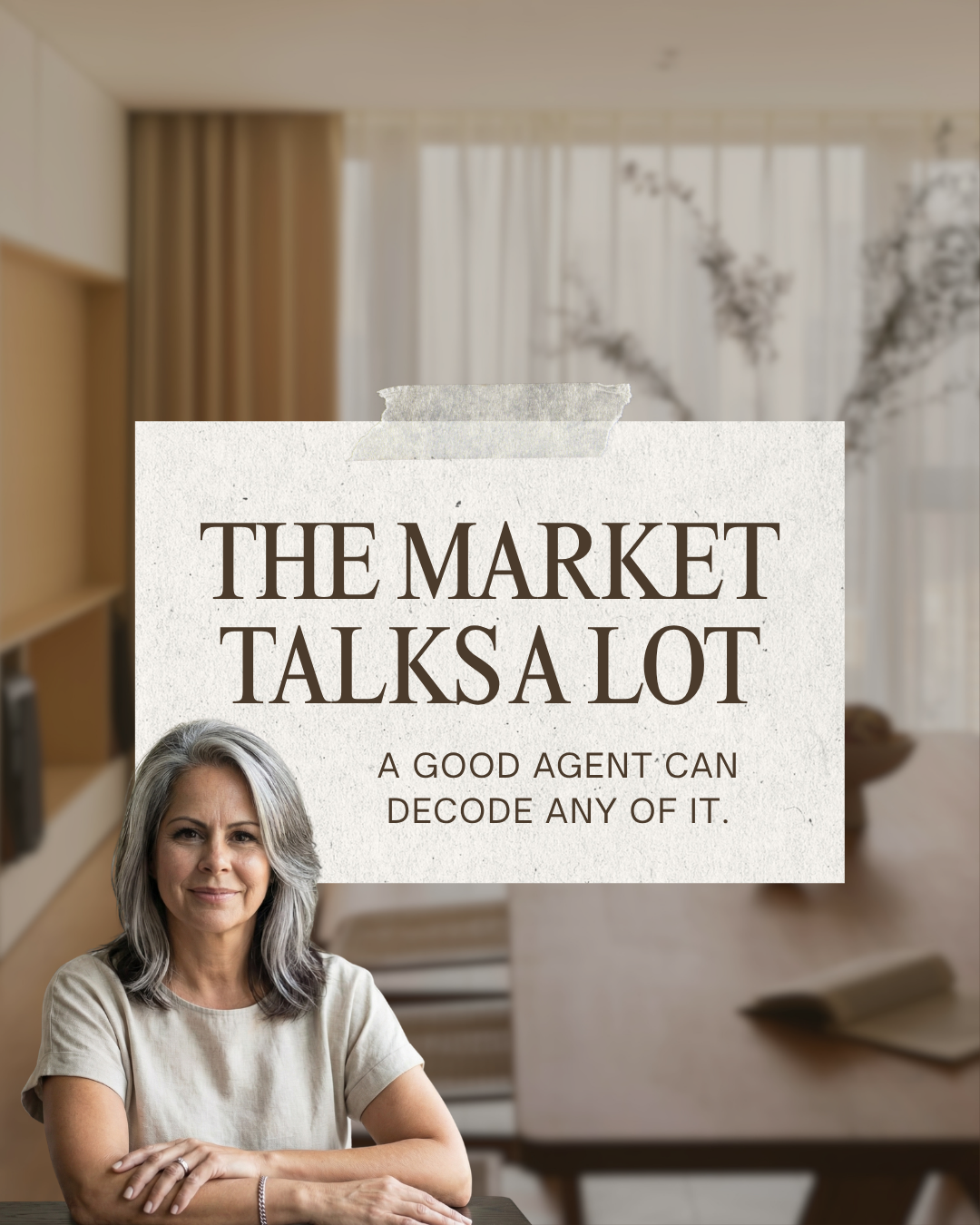 Leslie Huggins seated in a softly lit home beneath a paper sign reading The Market Talks a Lot and A Good Agent Can Decode Any of It